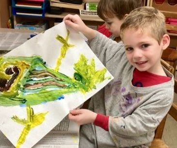 Two young boys are holding a piece of paper with a painting on it.