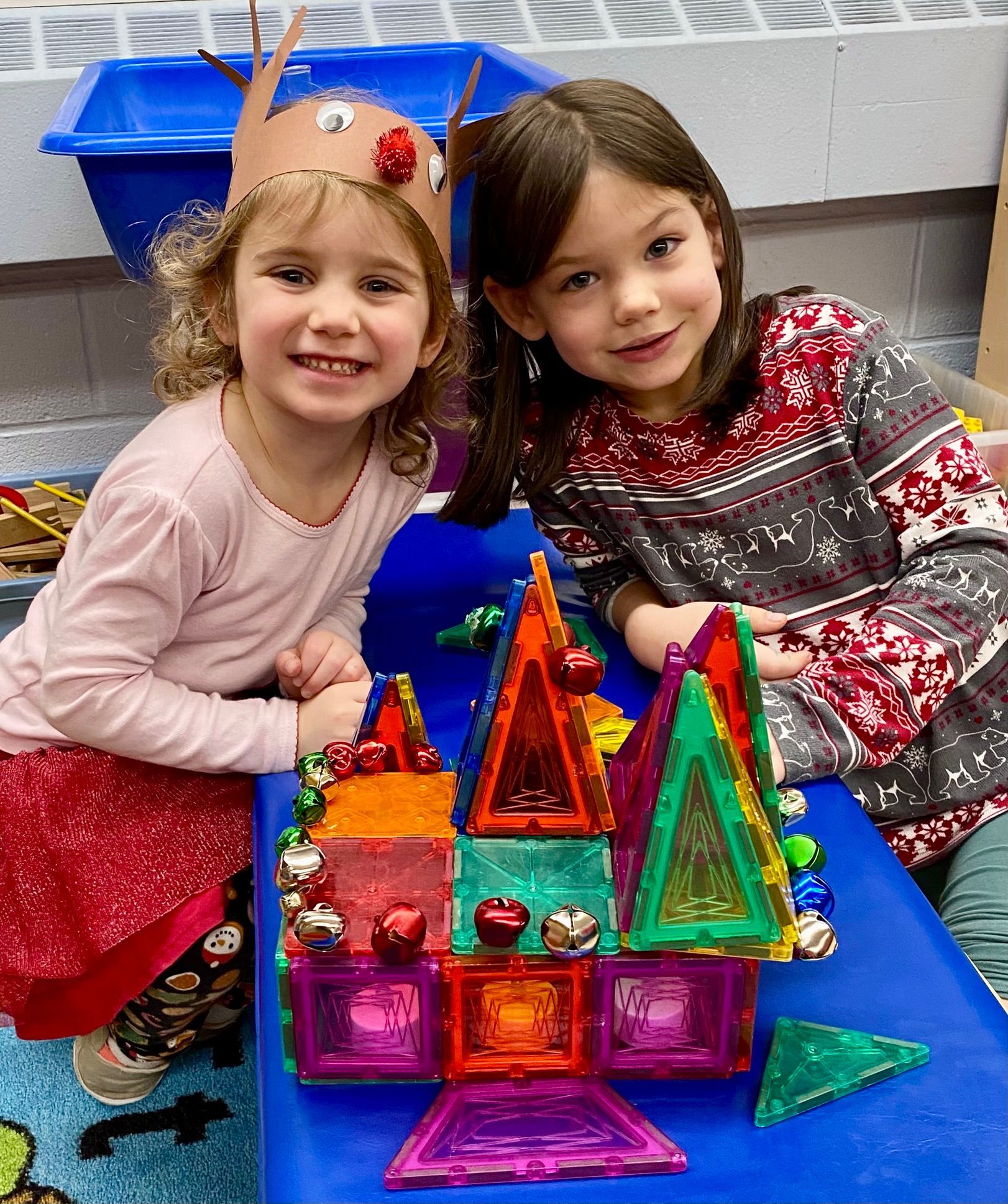 Two little girls are sitting at a table with a castle made out of magnets.