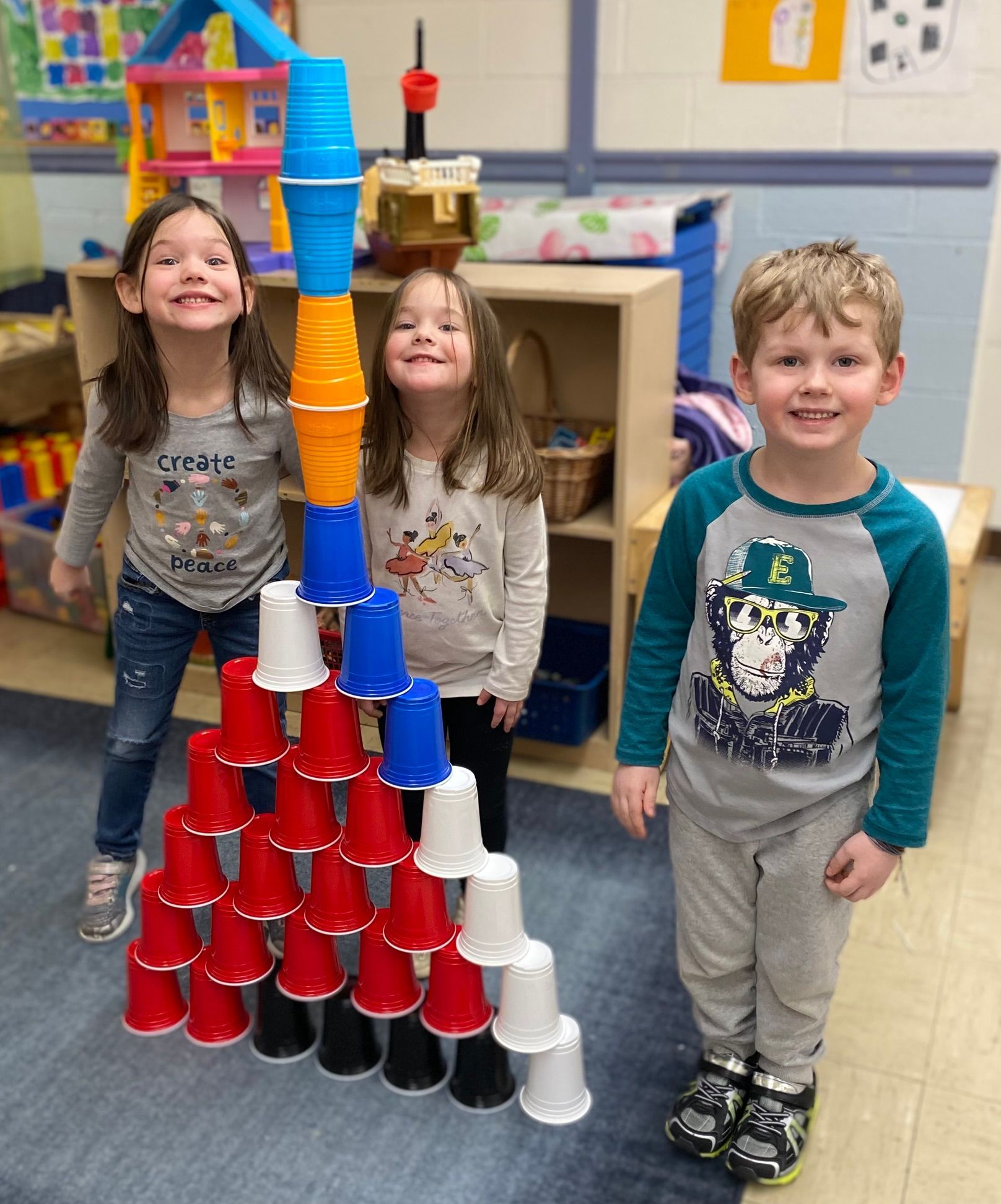 Three children are standing next to a stack of cups.
