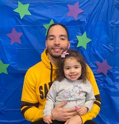 A man in a yellow sweatshirt is holding a little girl in his arms.