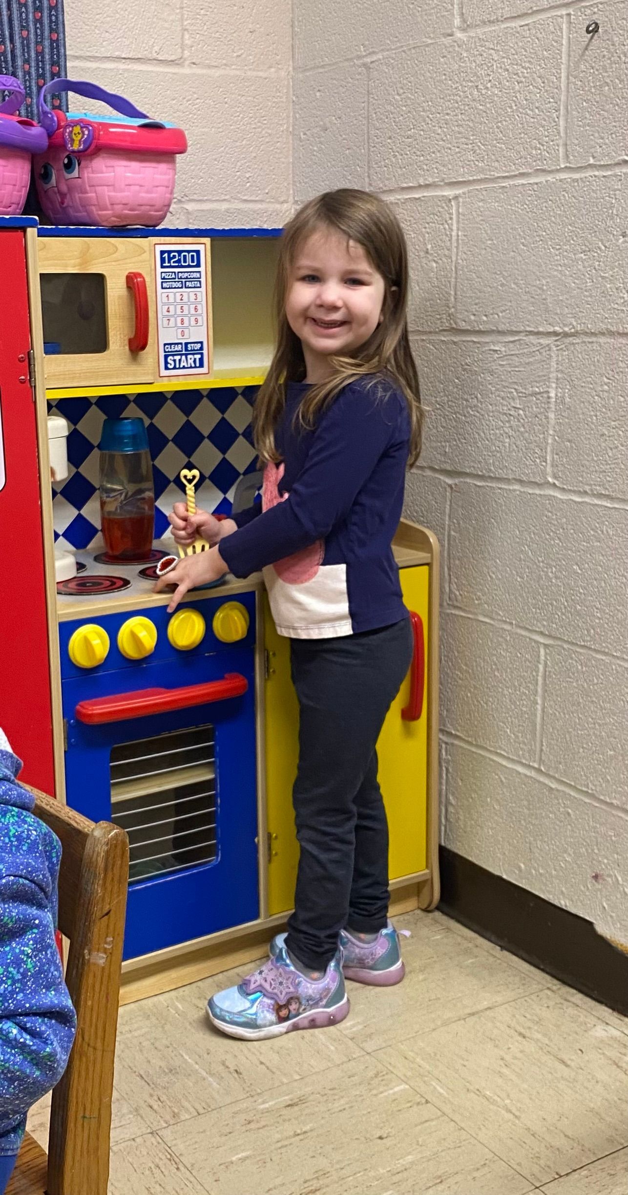 A little girl is standing in front of a toy kitchen.