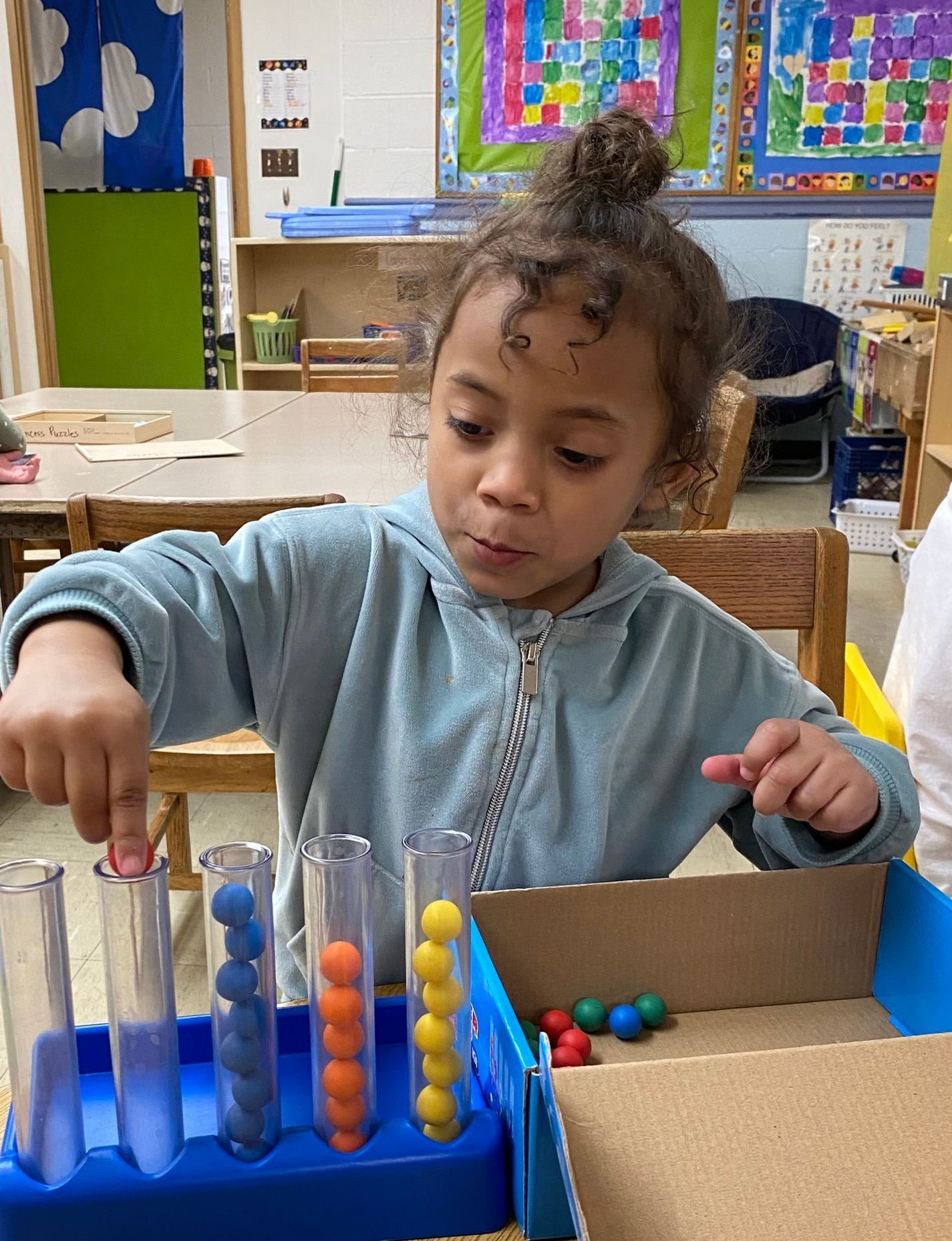 A little girl is playing with a toy in a classroom.