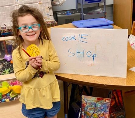 A little girl is standing in front of a sign that says cookie shop