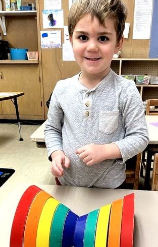 A young boy is sitting at a table with a rainbow made out of paper.