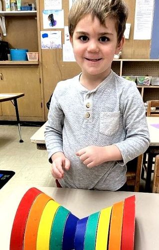 A young boy is sitting at a table with a rainbow made out of paper.