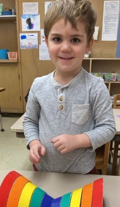 A young boy is sitting at a table with a rainbow craft.