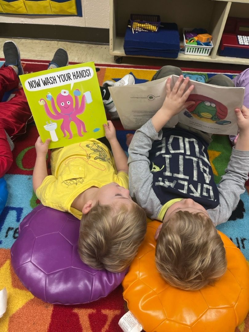 Two young boys are laying on the floor reading books