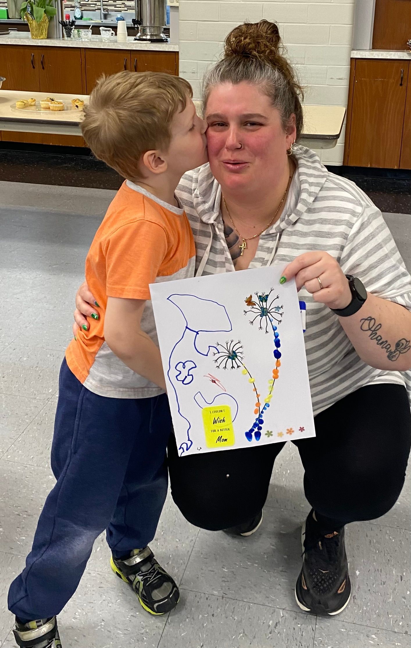A woman is kissing a child on the cheek while holding a drawing.