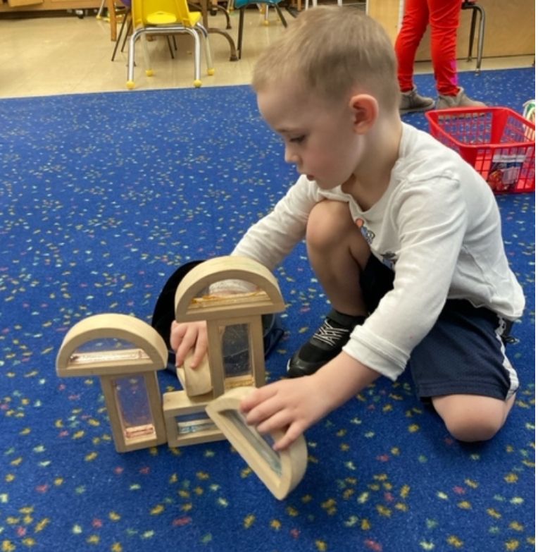 A young boy is kneeling on the floor playing with wooden blocks