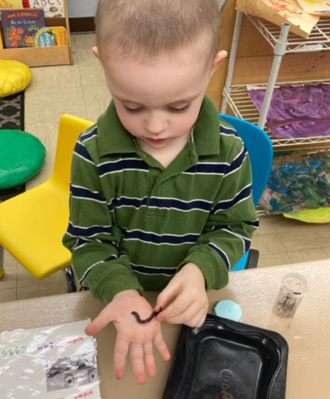 A young boy in a green striped shirt is playing with a worm on his hand