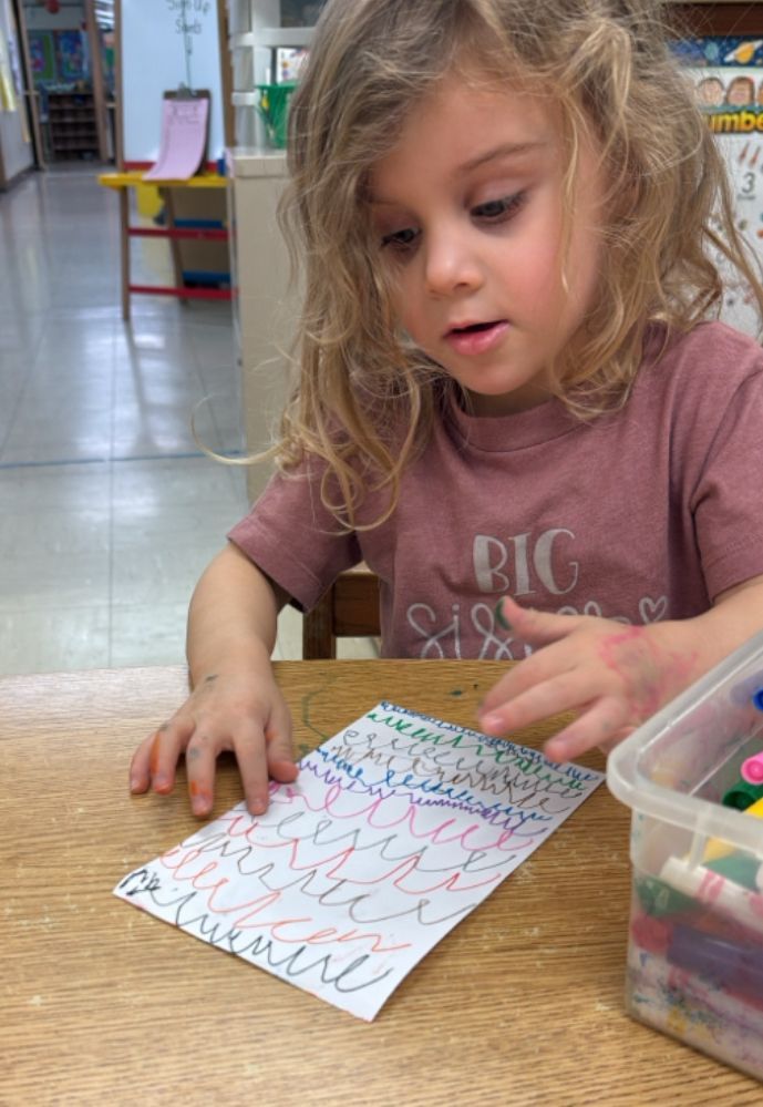 A little girl is sitting at a table playing with a piece of paper.