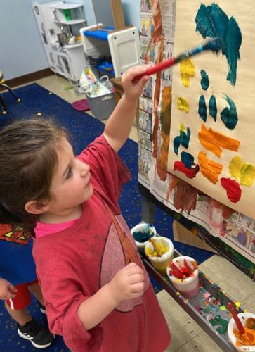 A little girl is painting on a wall with a brush