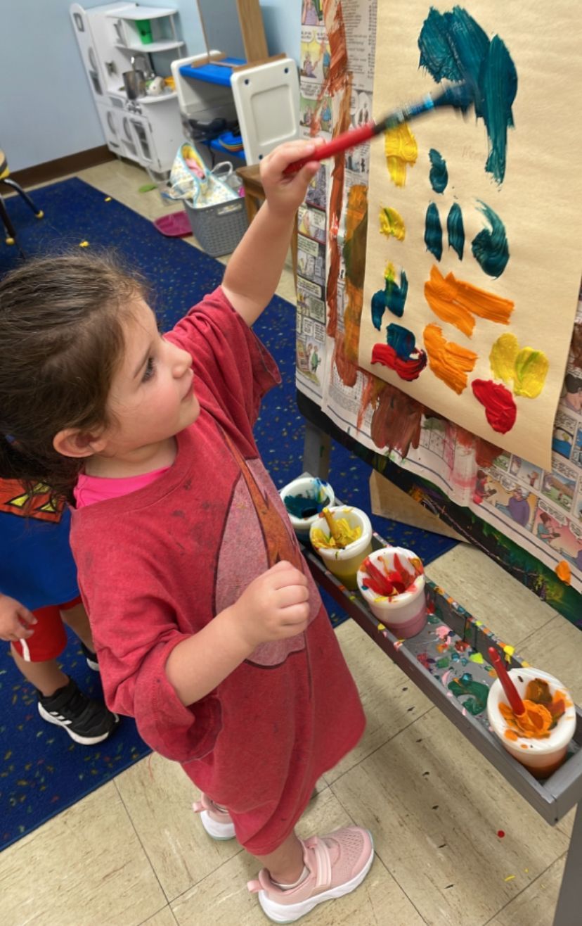 A little girl is painting on a canvas with a brush.