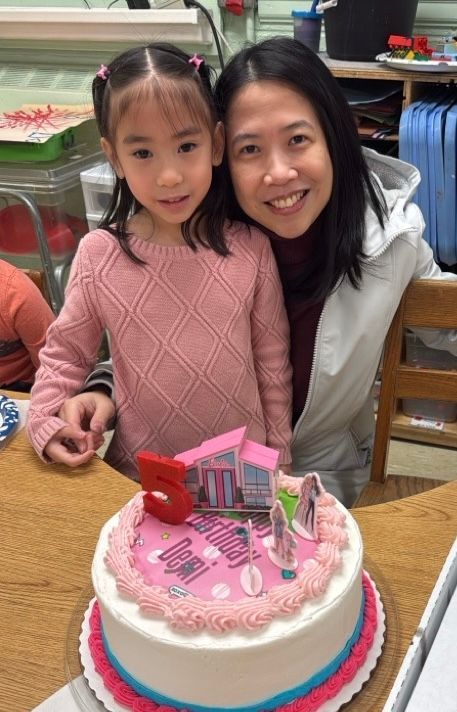 A woman and a little girl are posing for a picture in front of a birthday cake.
