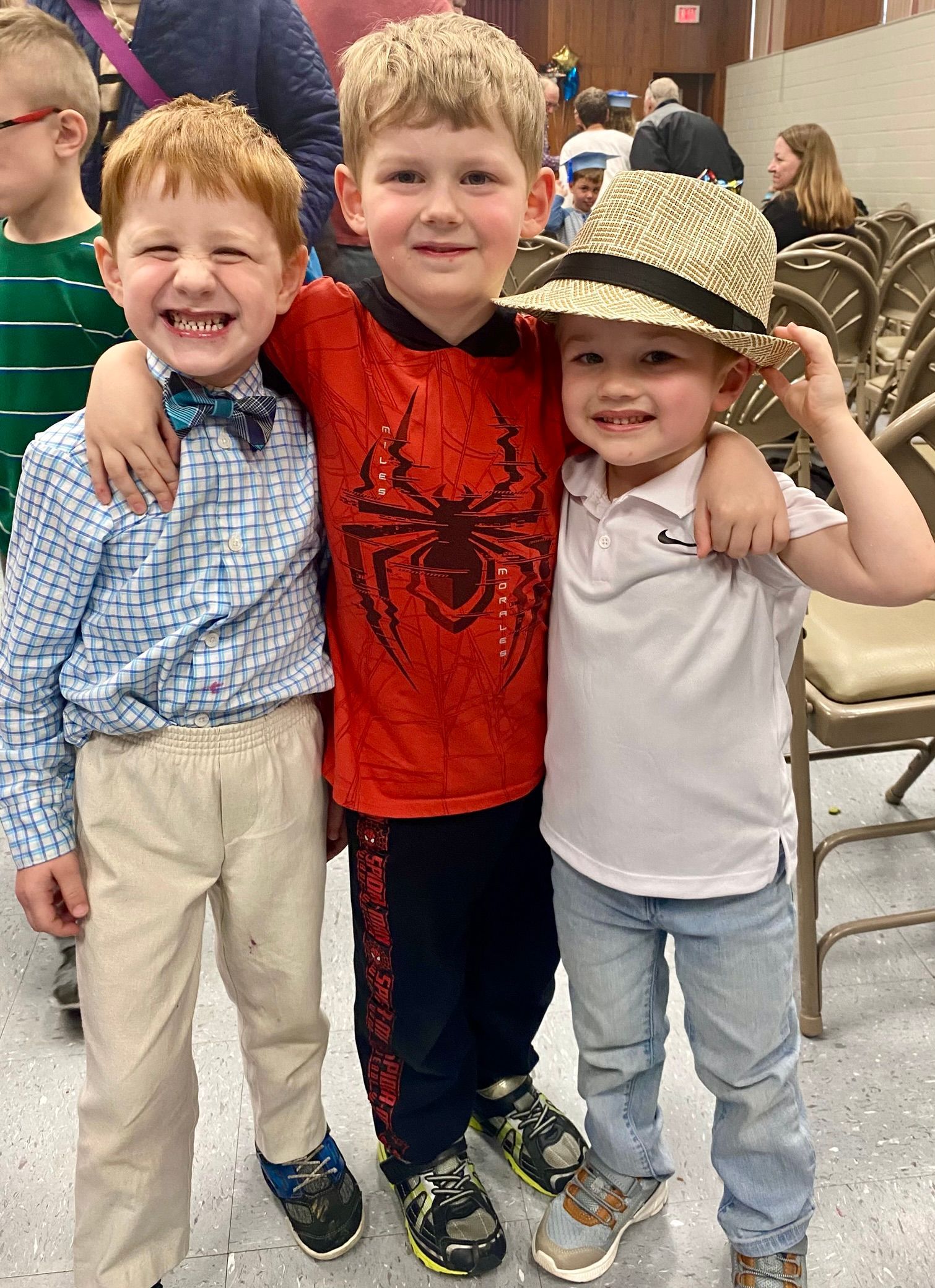 Three young boys are posing for a picture together . one of the boys is wearing a spiderman shirt.