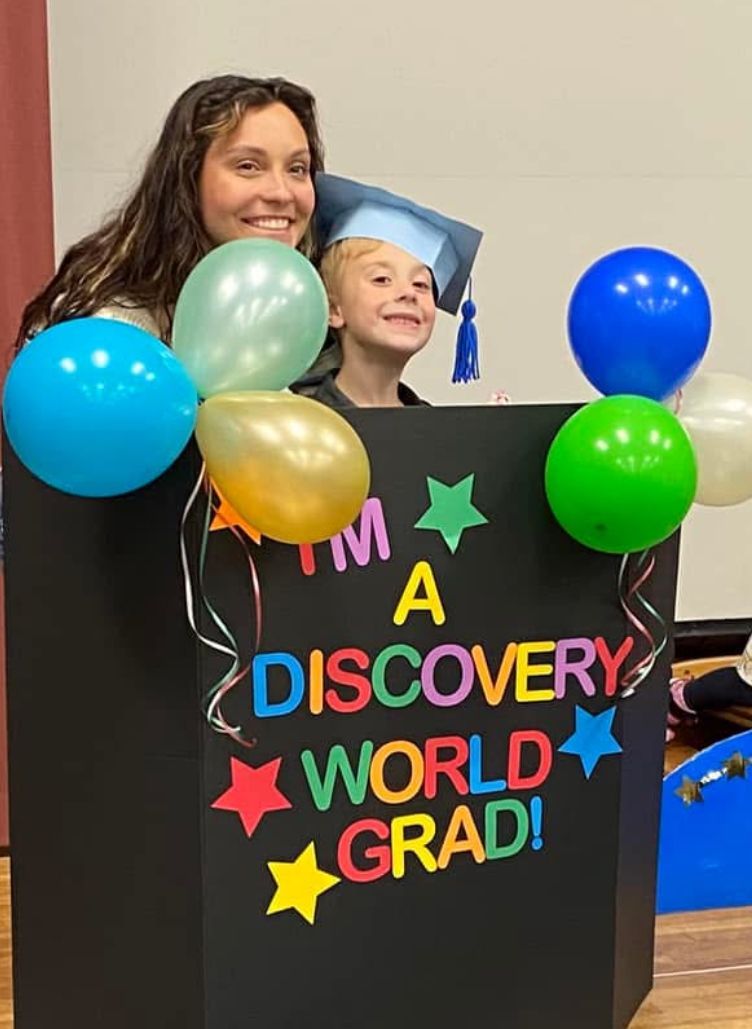 A woman and a child are standing behind a sign that says a discovery world grad.