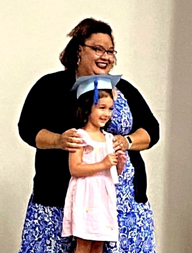 A woman is holding a little girl wearing a graduation cap.