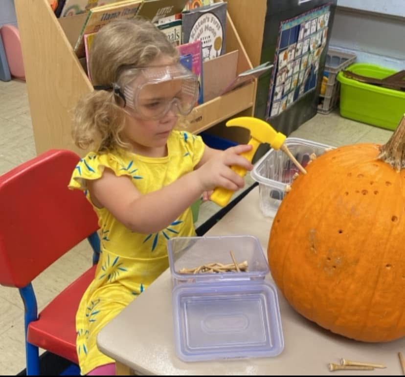 A little girl wearing goggles is playing with a pumpkin
