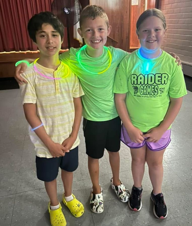 Three children wearing neon glow in the dark necklaces are posing for a picture.