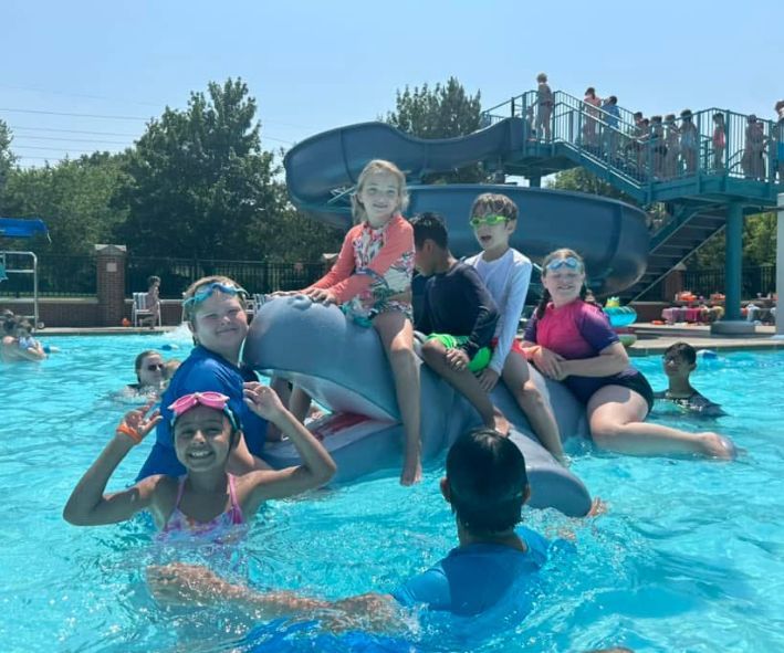 A group of children are sitting on a dolphin in a swimming pool.