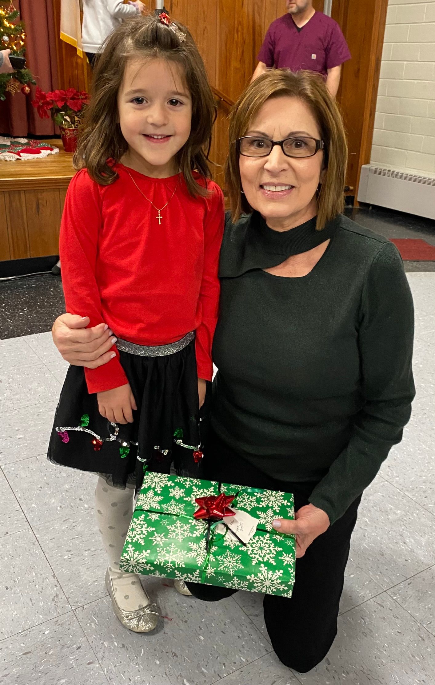 A woman is kneeling down next to a little girl holding a gift box.