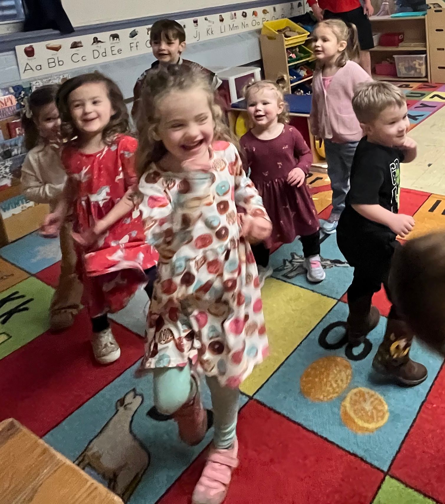 A group of children are standing on a rug in a classroom.