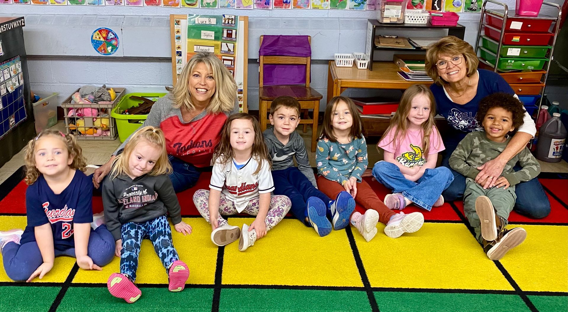 A group of children are sitting on the floor in a classroom.
