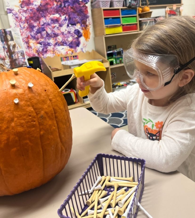 A little girl wearing goggles is playing with a pumpkin