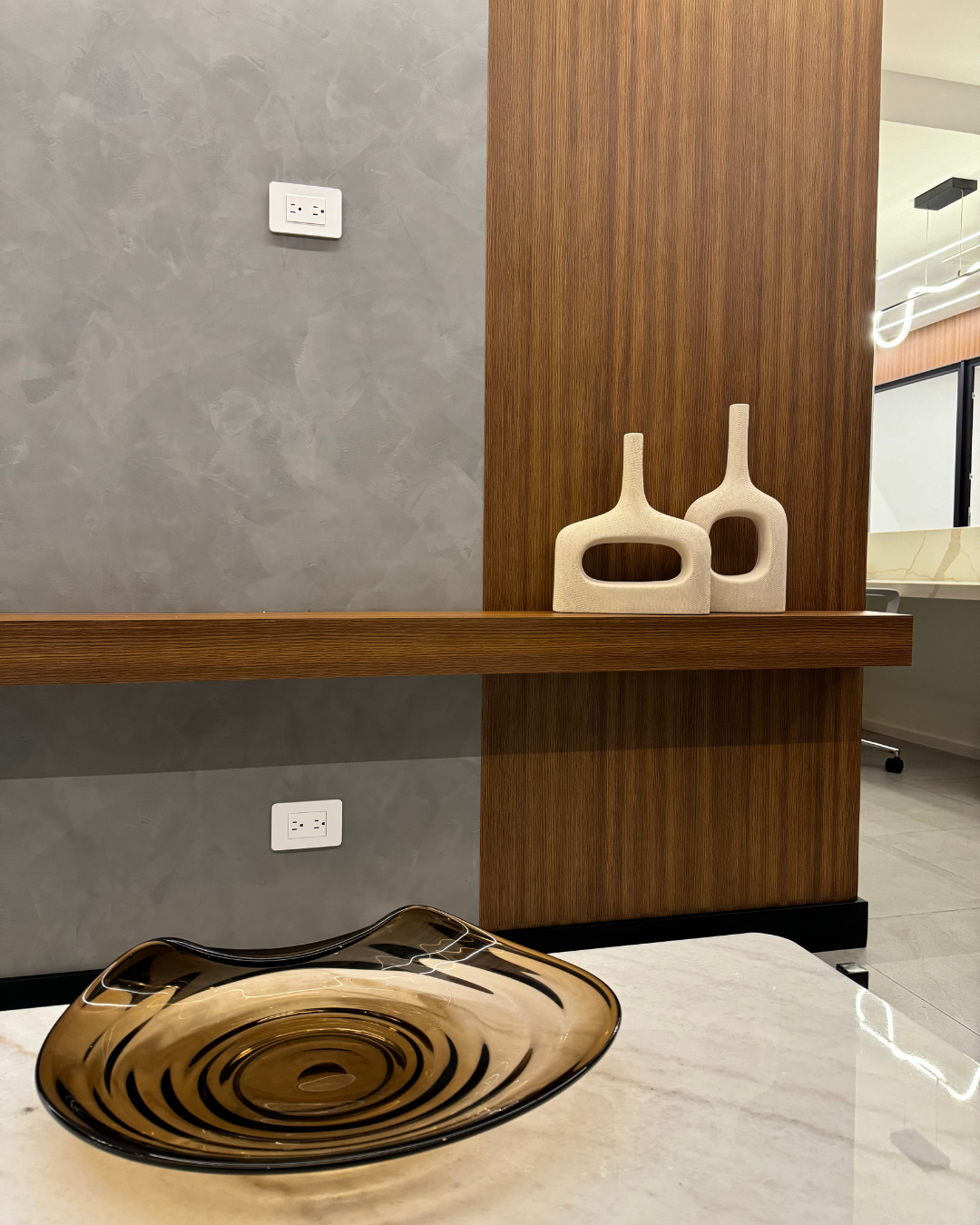 Hay un cuenco sobre una mesa al lado de una pared con dos jarrones encima.