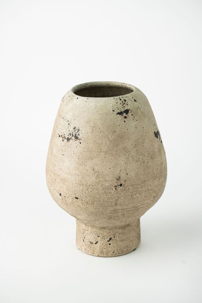 Un jarrón de cerámica reposa sobre una superficie blanca.