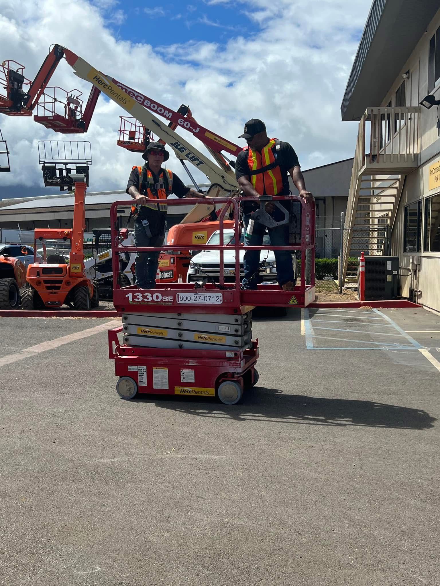 Two construction workers in orange vests operate a red scissor lift outdoors near a building. The sky is blue with clouds.