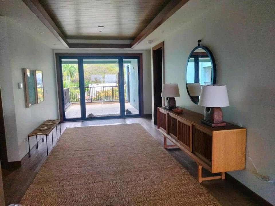 A hallway with a large rug, wooden console table with lamps, a mirror, and a glass door leading to a balcony.