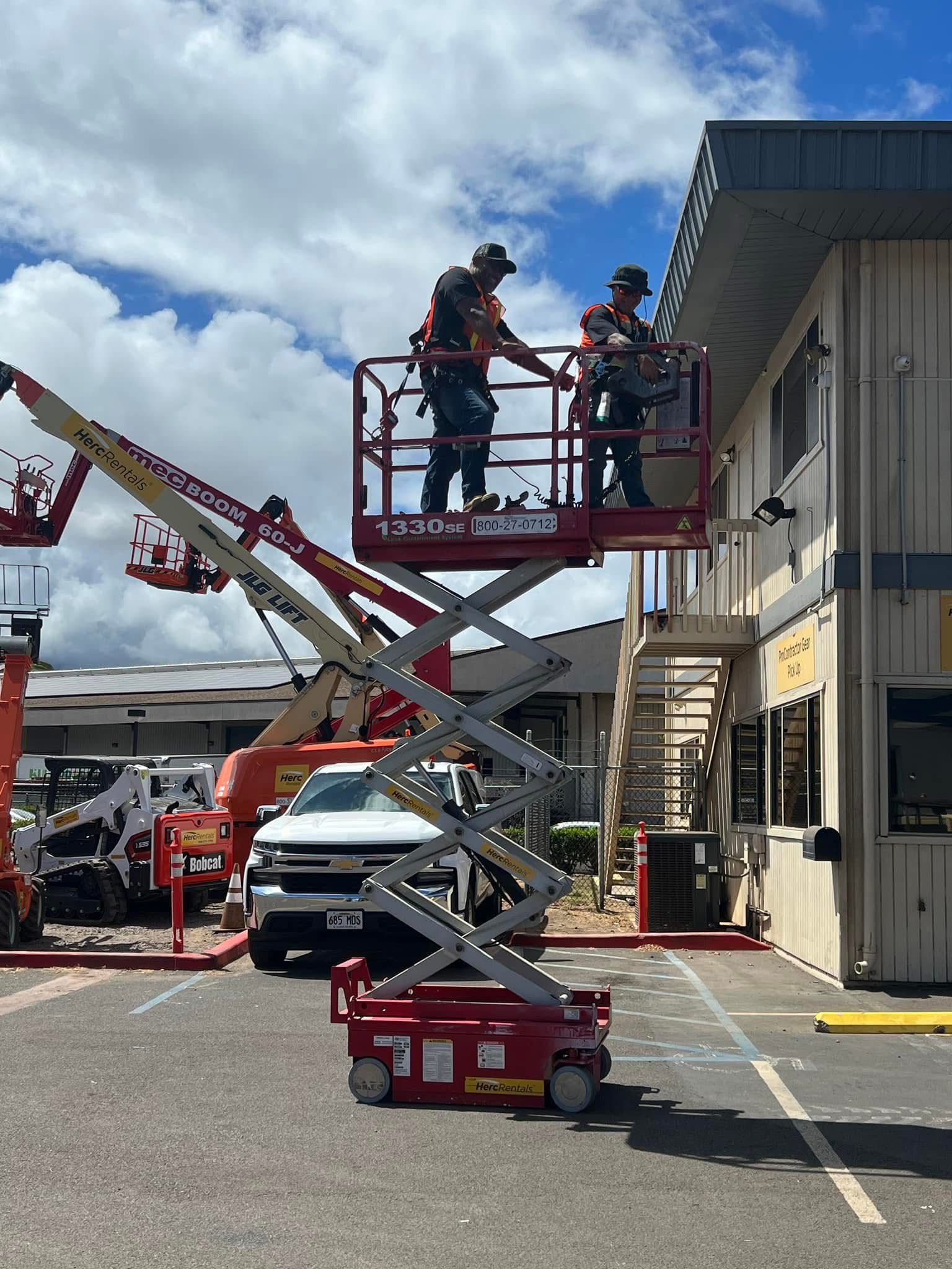 Two workers in a lift platform near a building, presumably working on the exterior. Bright, sunny day.