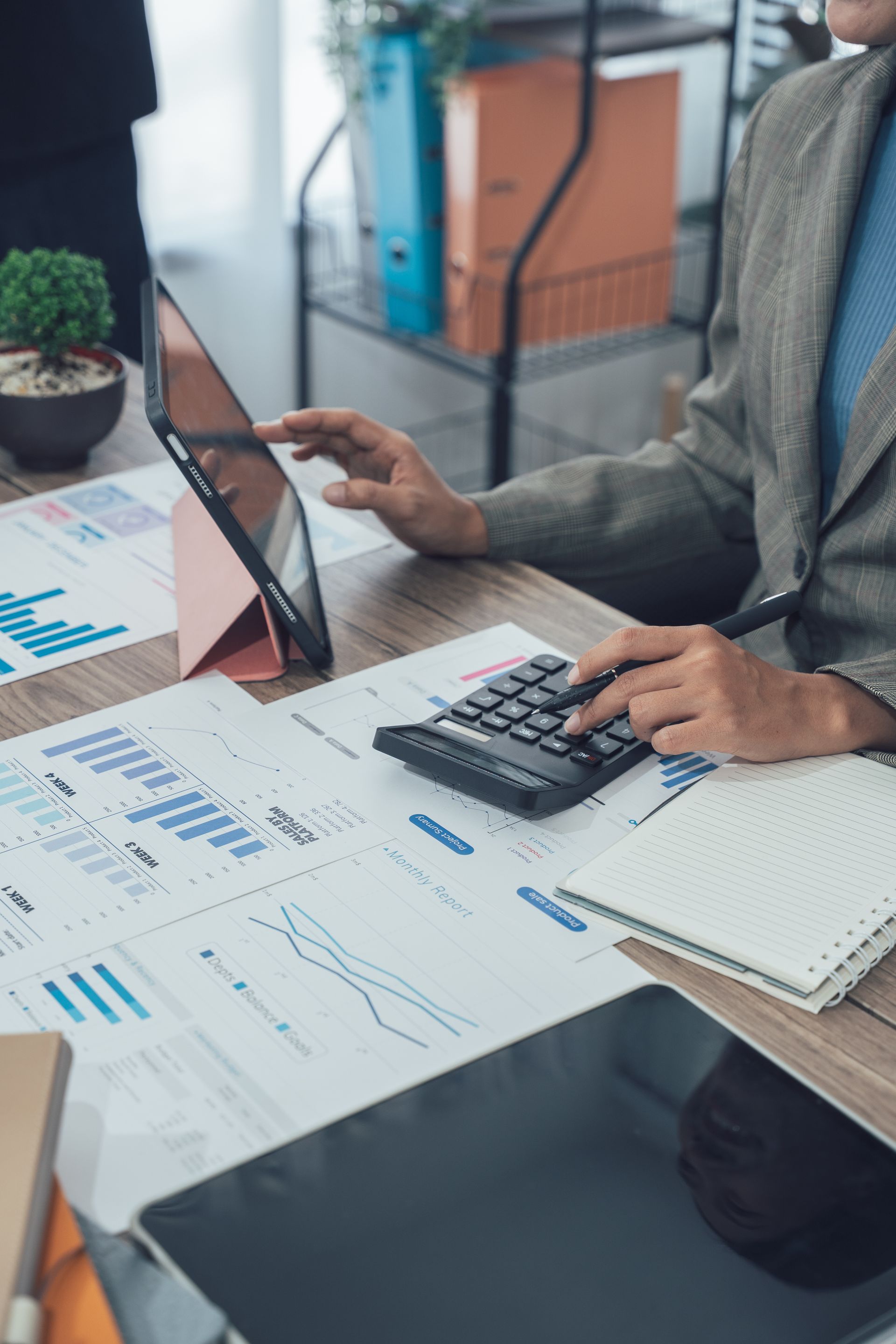 Person using a calculator and tablet at a desk with financial documents.