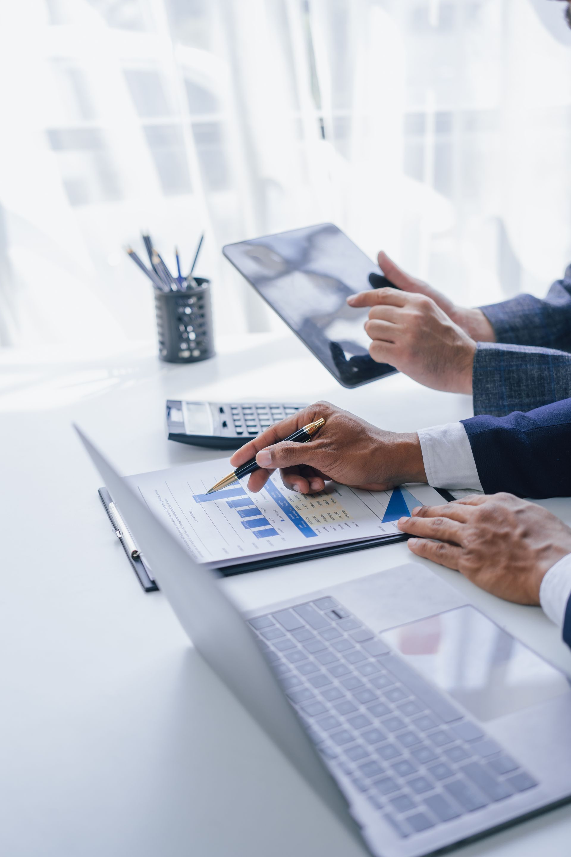 Two people reviewing financial data at a desk, one using a tablet, the other pointing at a graph on a report.