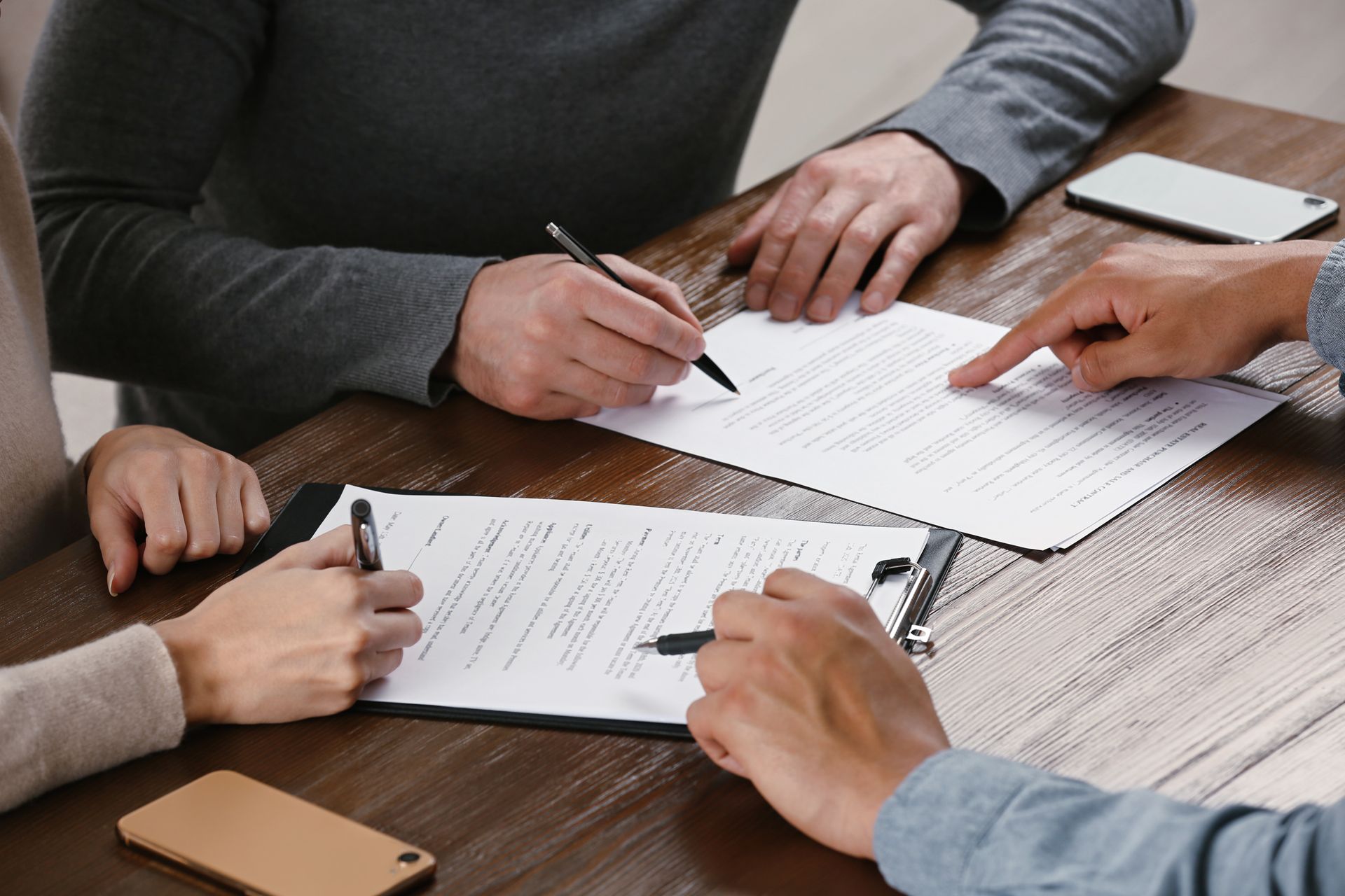 People signing documents at a table; one person points at a page.