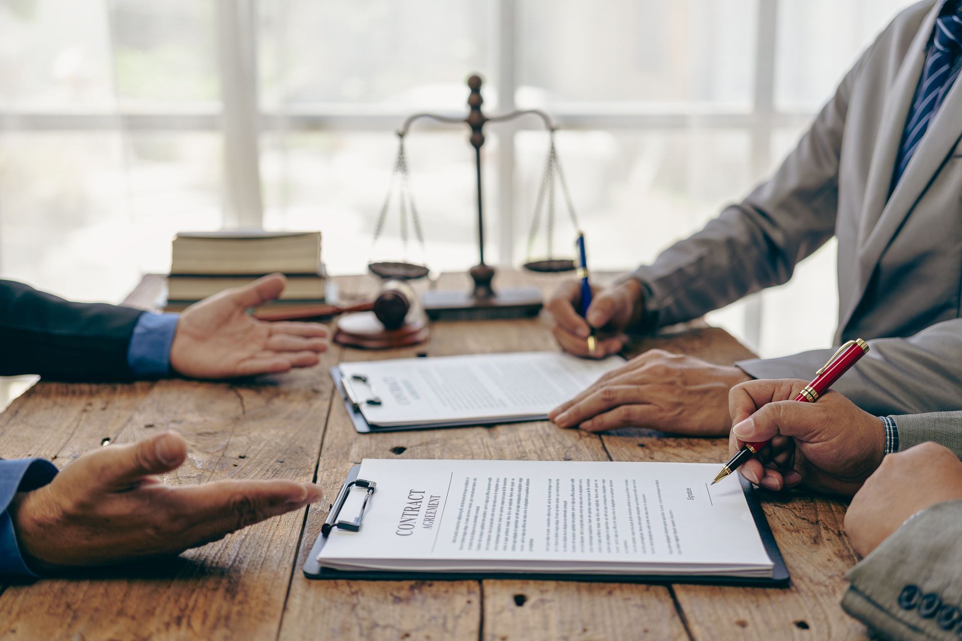 Lawyers at a wooden table signing documents; scales of justice and books are in the background.