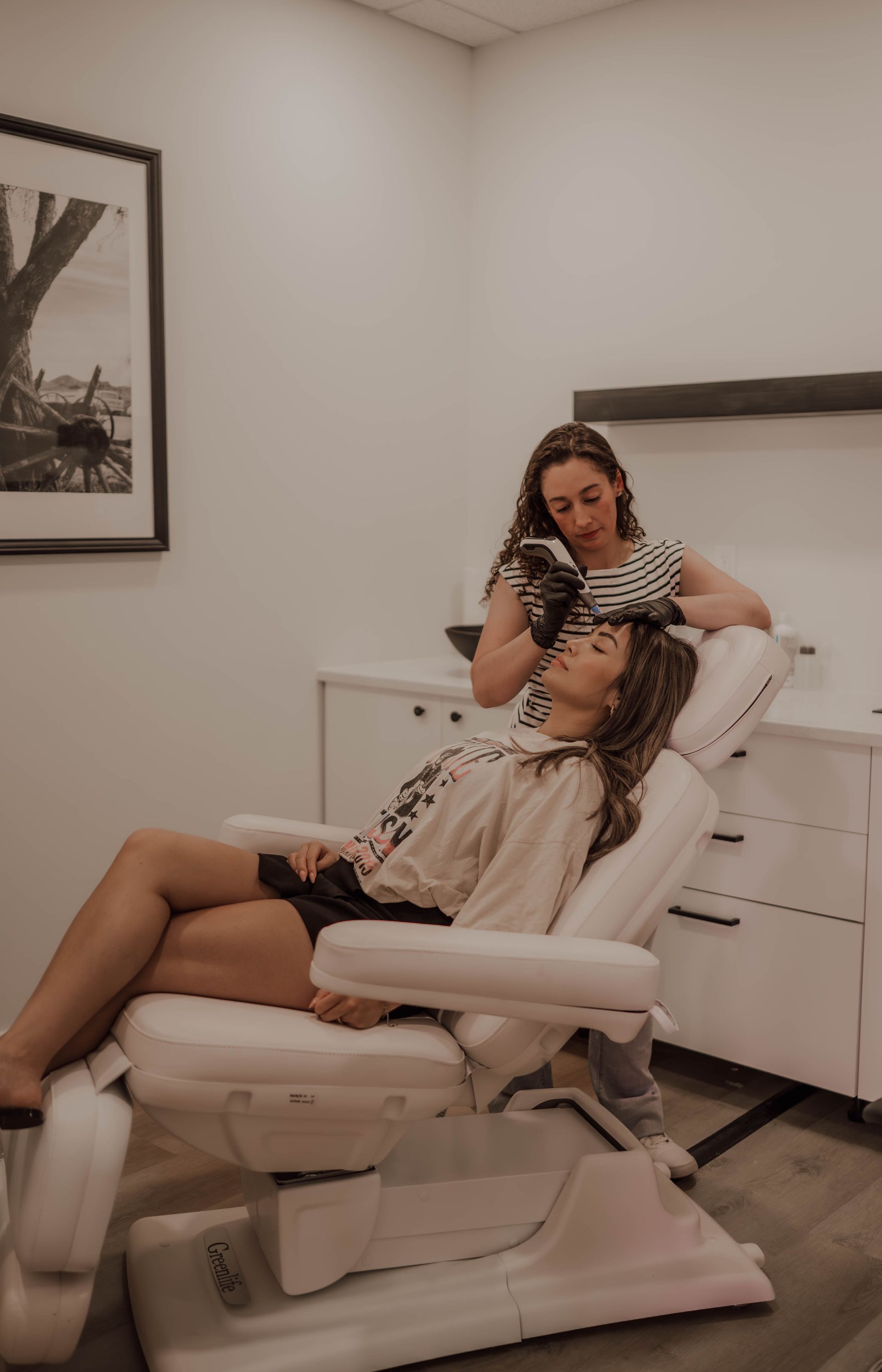 A woman is sitting in a chair getting a facial treatment.