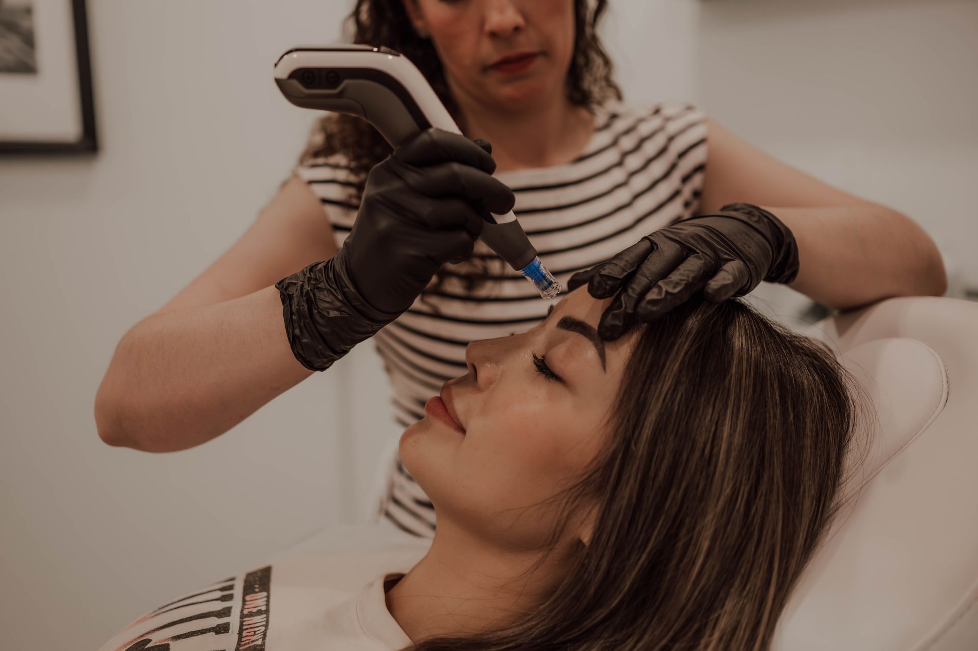 A woman is getting a tattoo on her eyebrows.