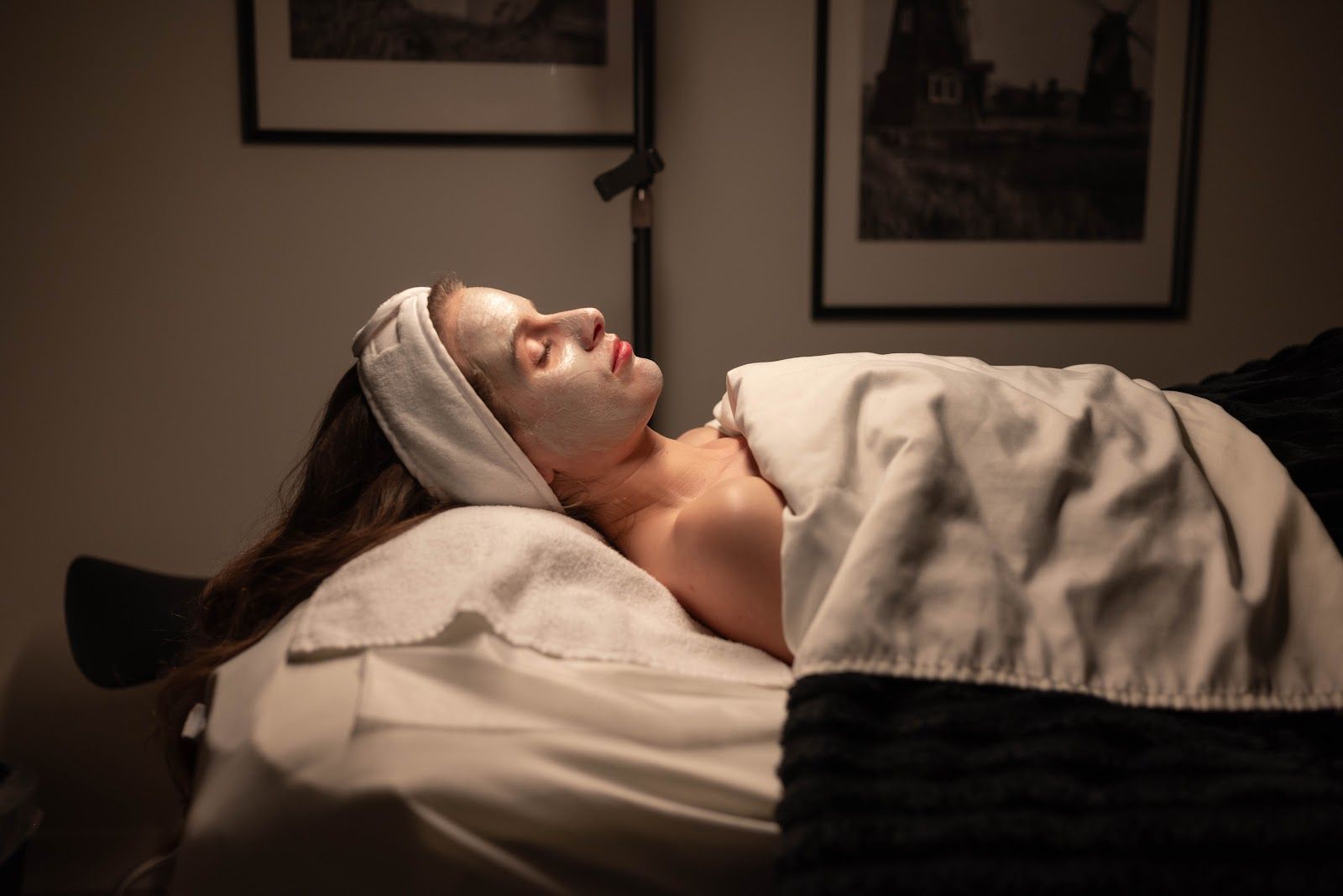 Person lying on a massage table with a facial mask. Face is covered, with a white towel on her head.