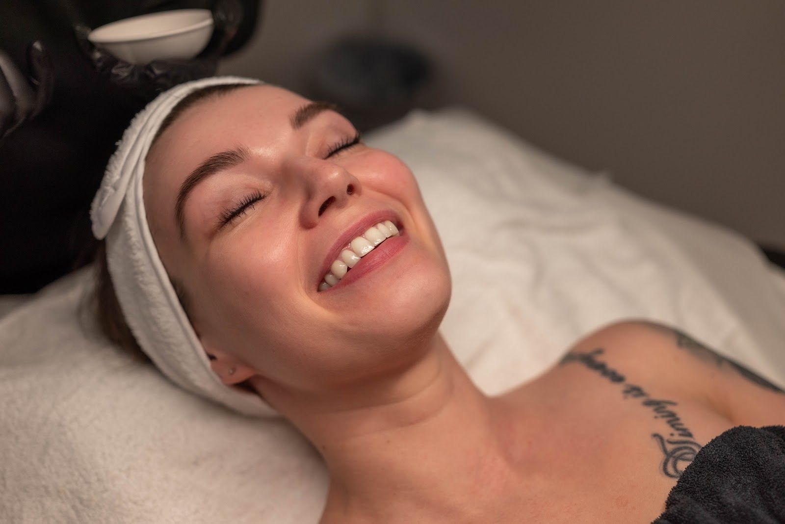 Woman smiling during a facial treatment, lying on a spa bed, receiving product application.