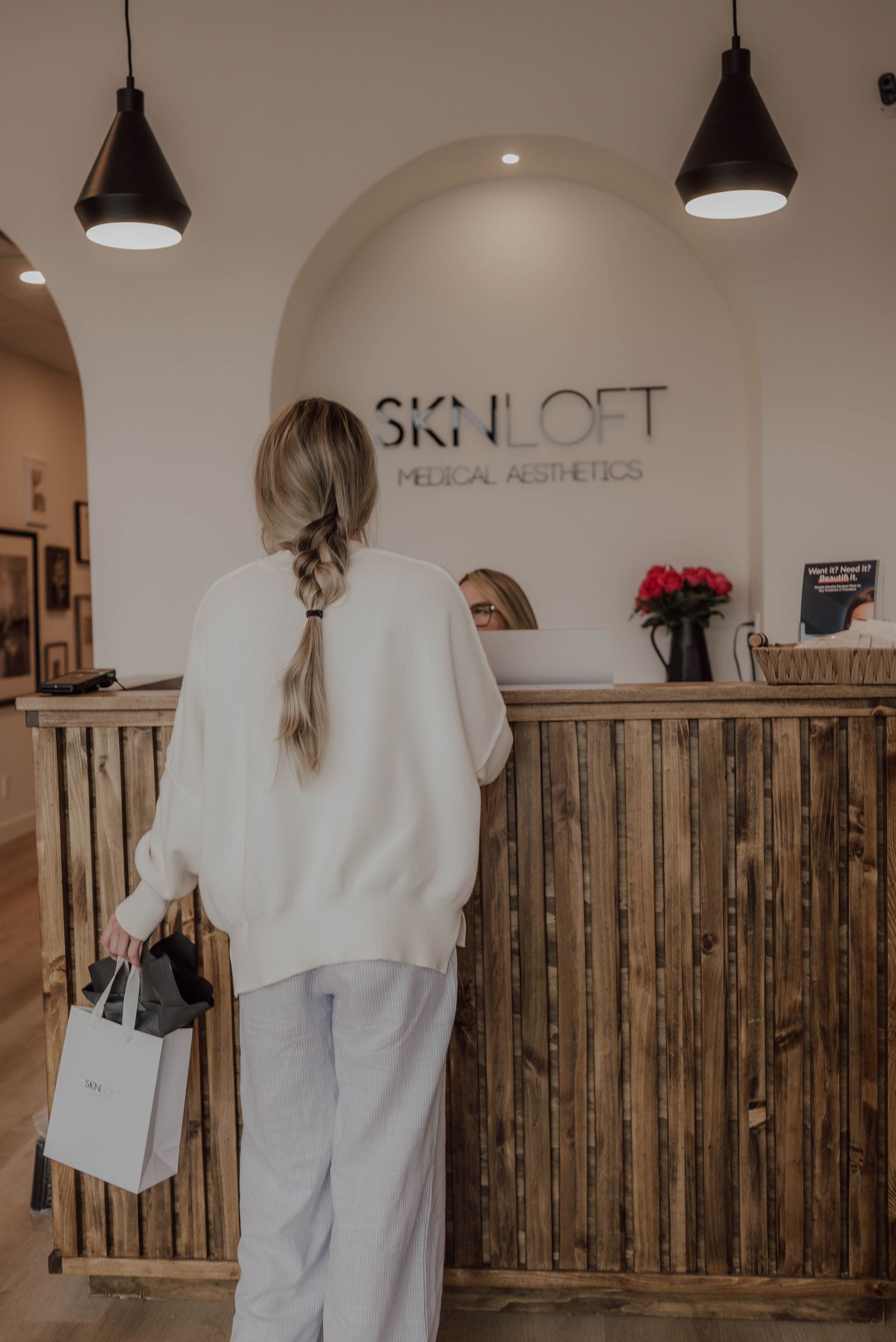A woman is standing at a counter in a salon holding shopping bags.