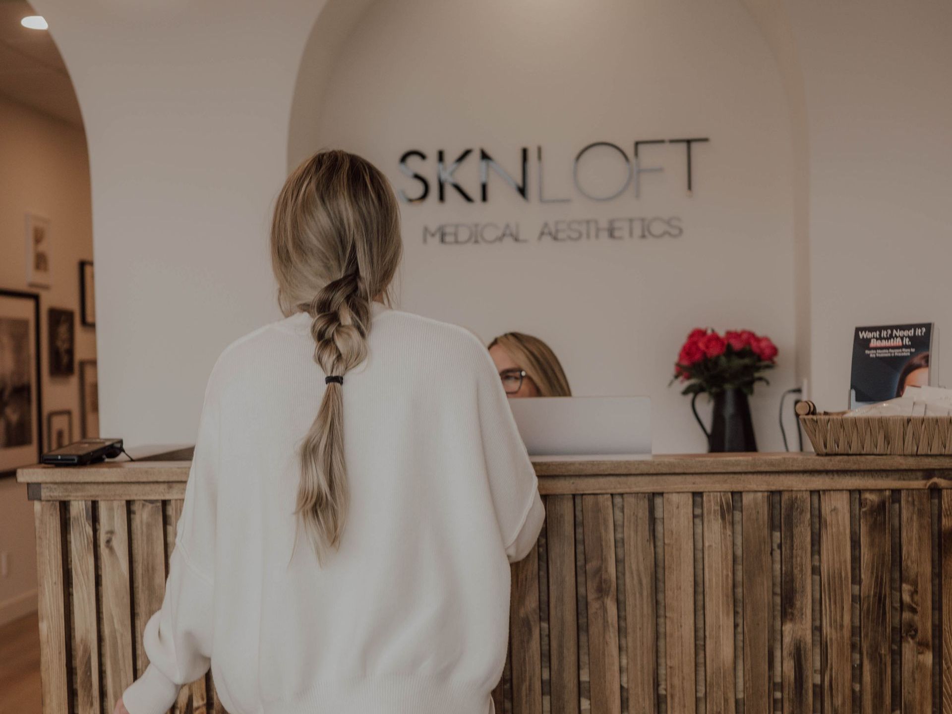 A woman is standing at a counter in front of a sign that says skin loft medical aesthetics.