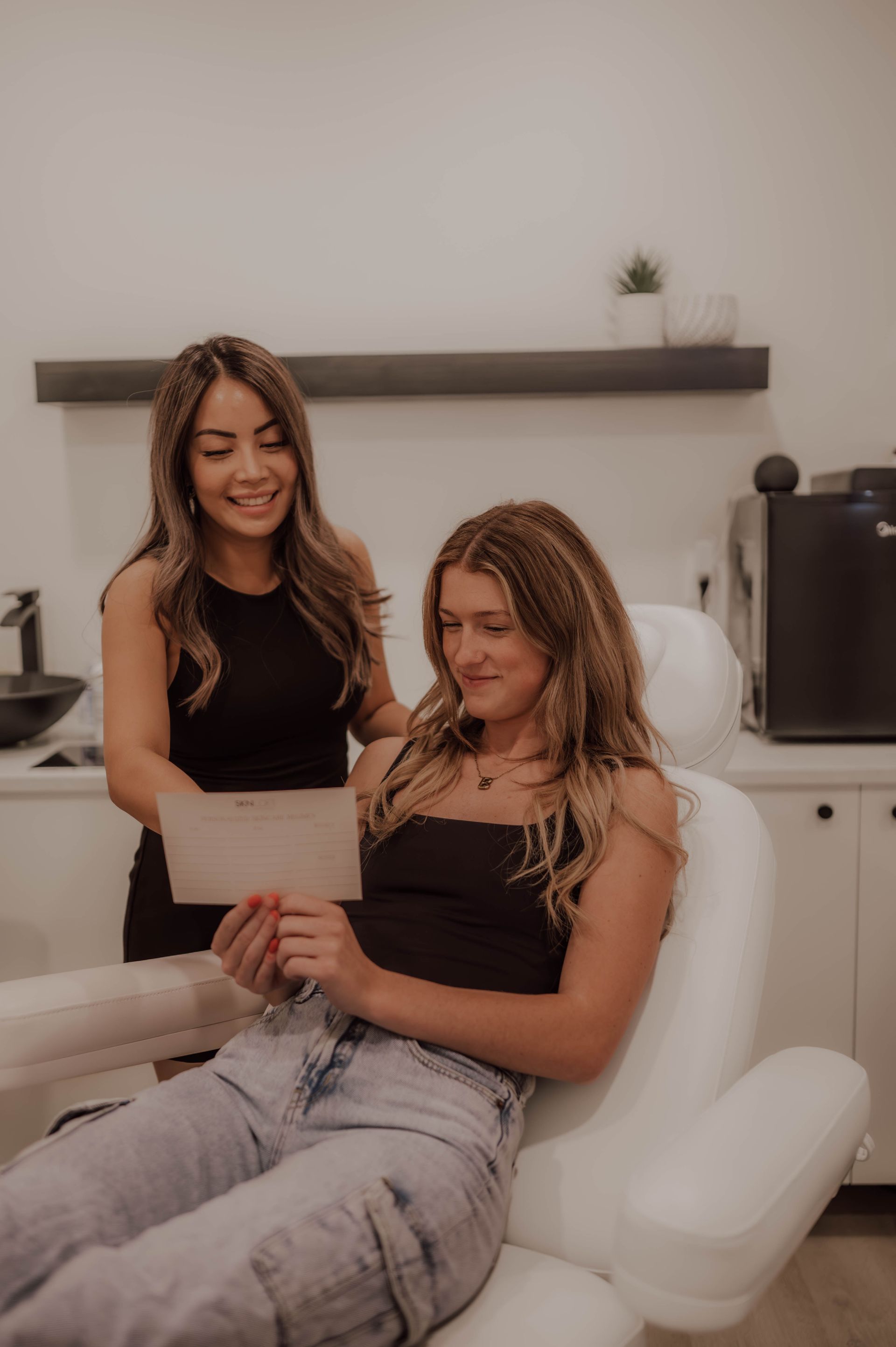 A woman is sitting in a chair while a woman stands behind her.