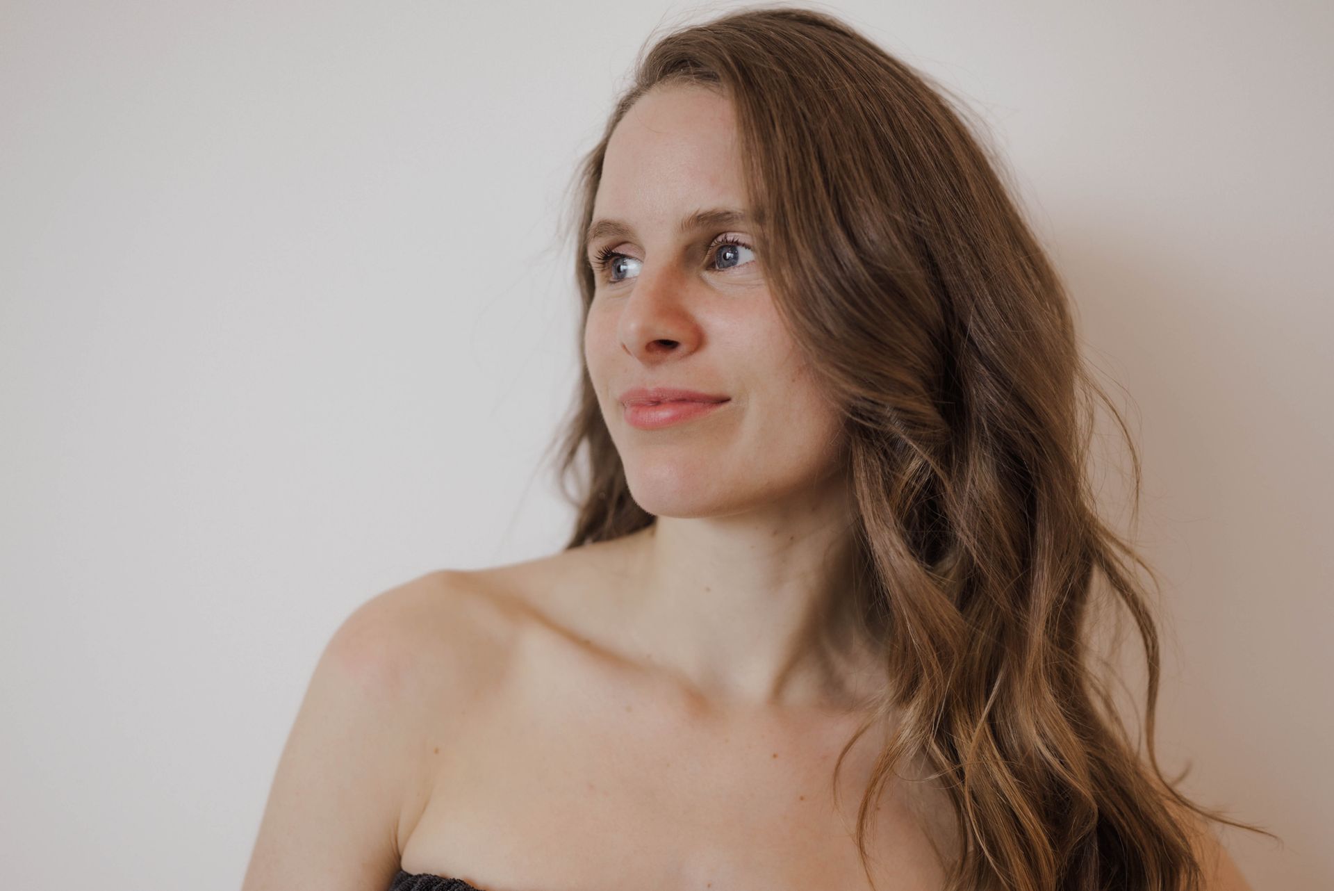 A woman with long brown hair is standing in front of a white wall.