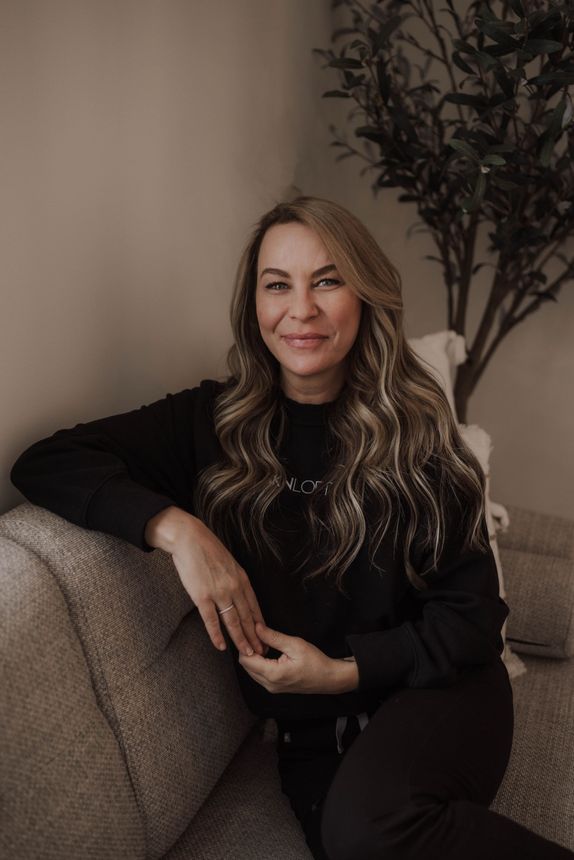 A woman is sitting on a couch with her legs crossed and smiling.