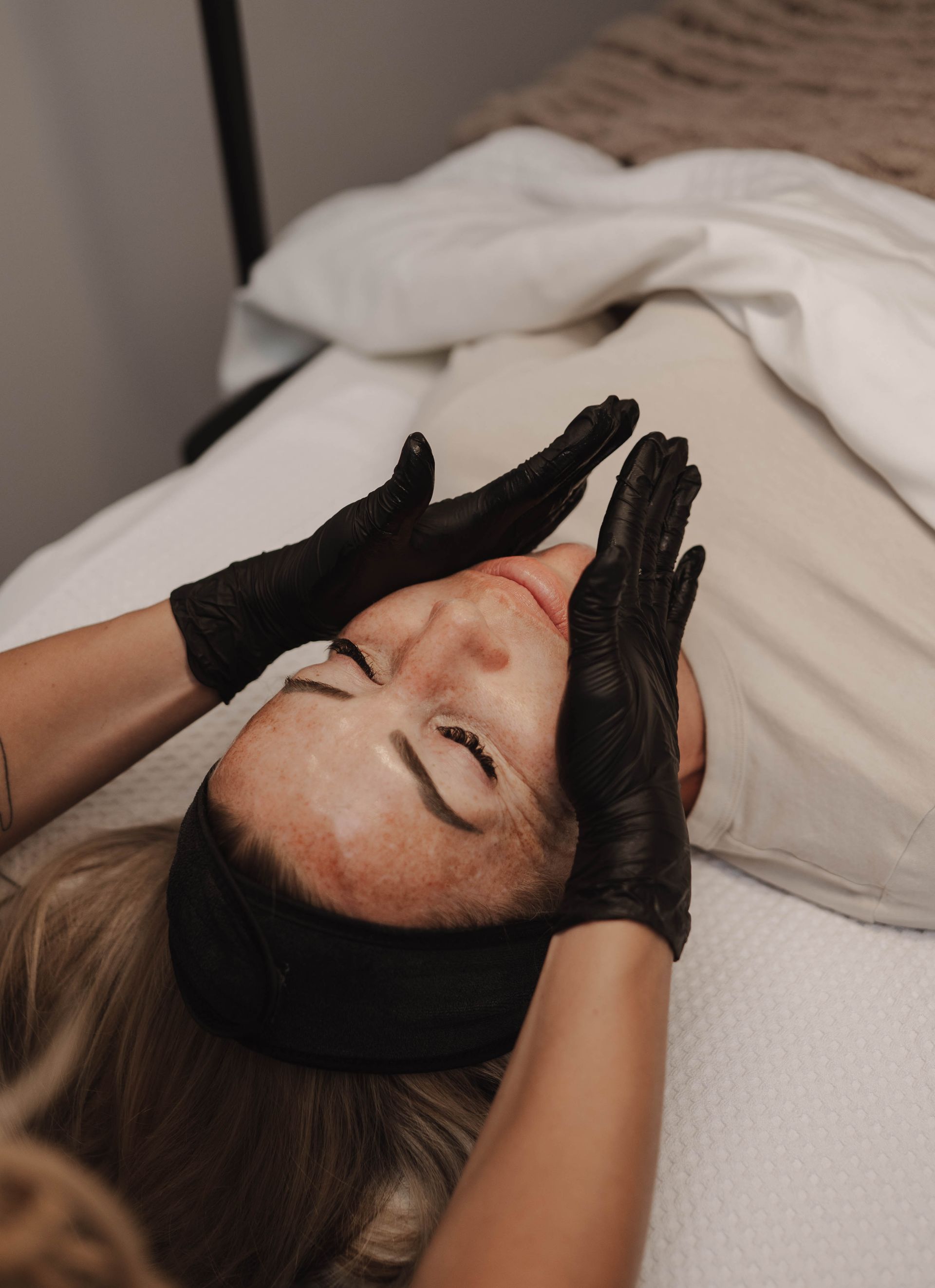 Person receiving facial treatment; gloved hands on face in spa setting.