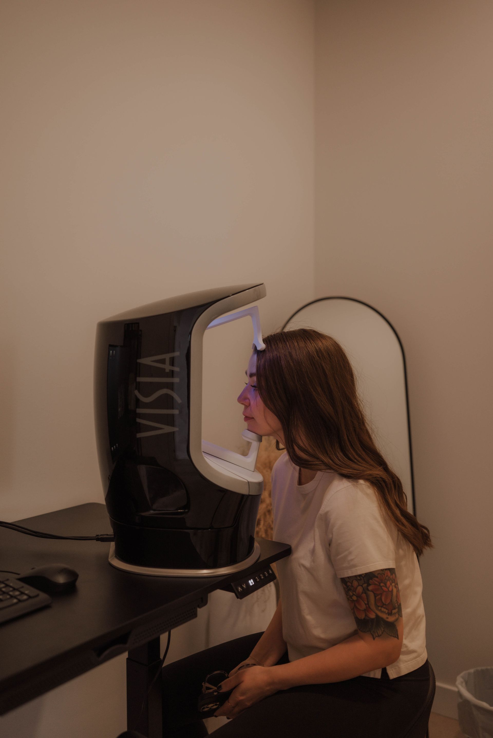 Woman using a VISTA skin analysis machine; she sits at a desk with a computer in a clinic.