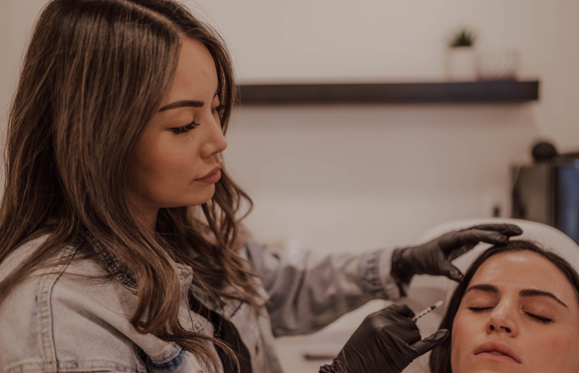 Woman giving a facial injection to a patient in a medical office setting. Both are wearing gloves.