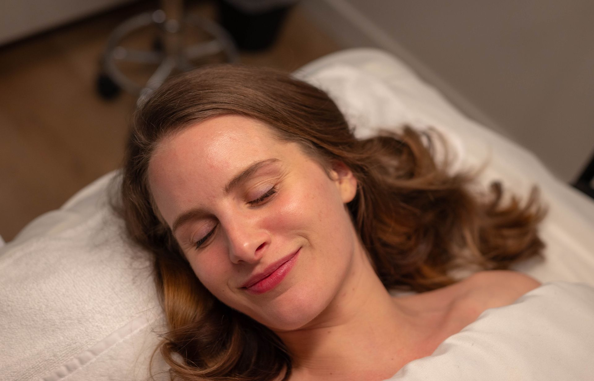 A woman is laying on a bed with her eyes closed and smiling.